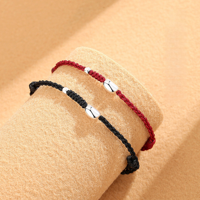 Close-up of red and black 925 silver jequirity bean bracelets displayed on a soft beige surface, showcasing their intricate woven design.