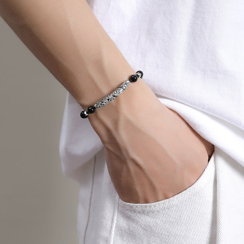 Black Onyx beaded hand rope with silver Xiangyun carving, worn on a wrist, showcasing its elegant and retro style.